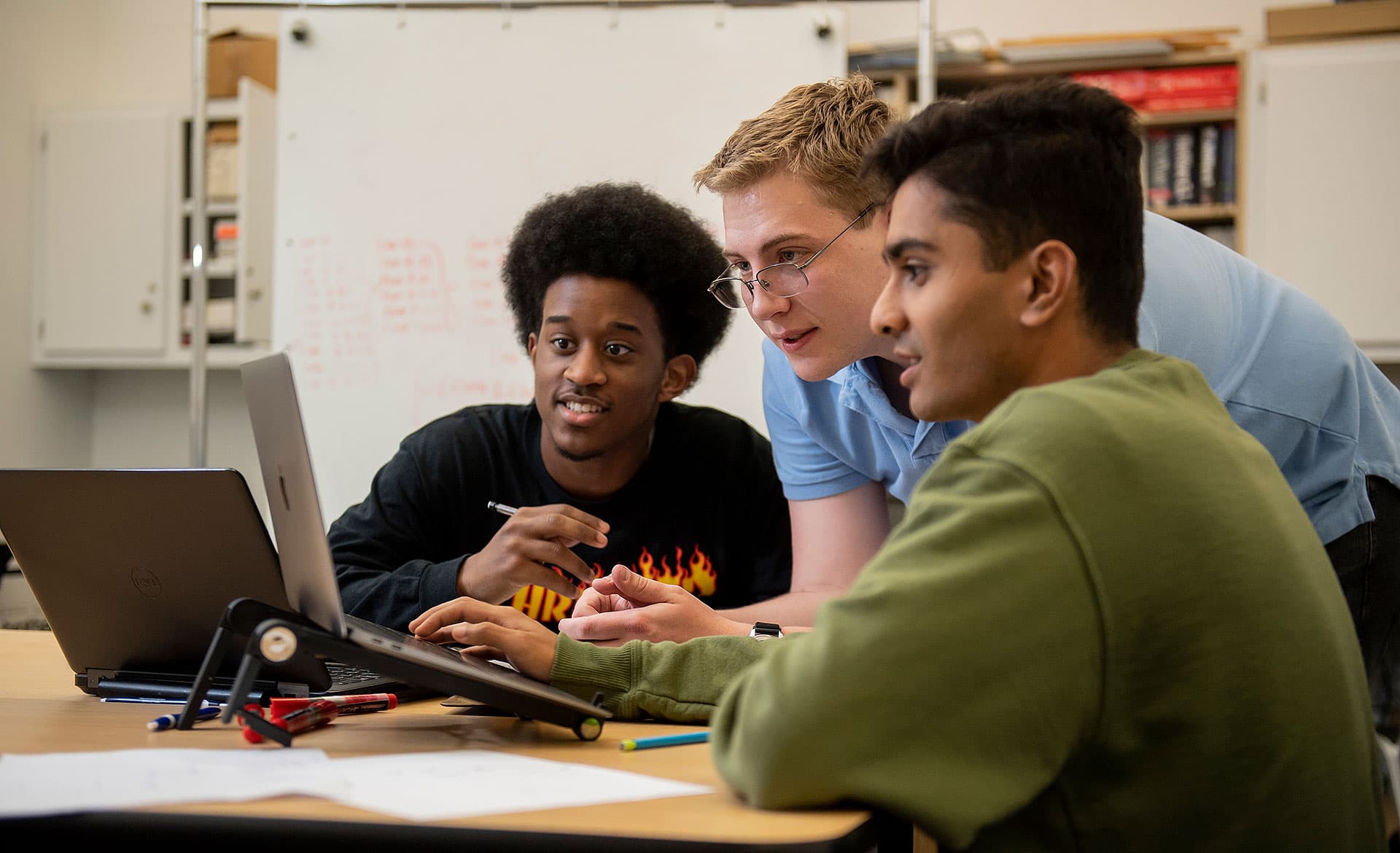 Three male students looking at a laptop in a classroom