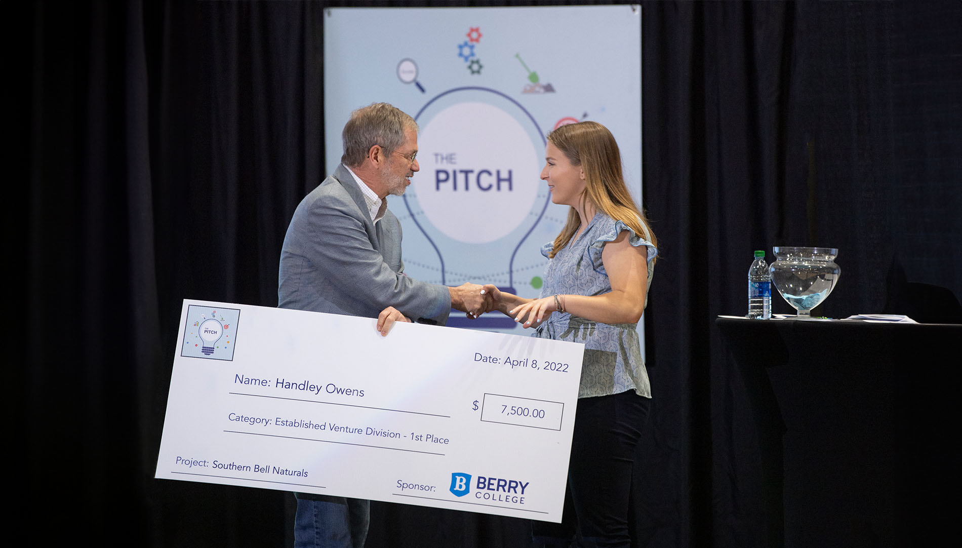 Berry College President Stephen Briggs presenting a large, promotional check to a female student