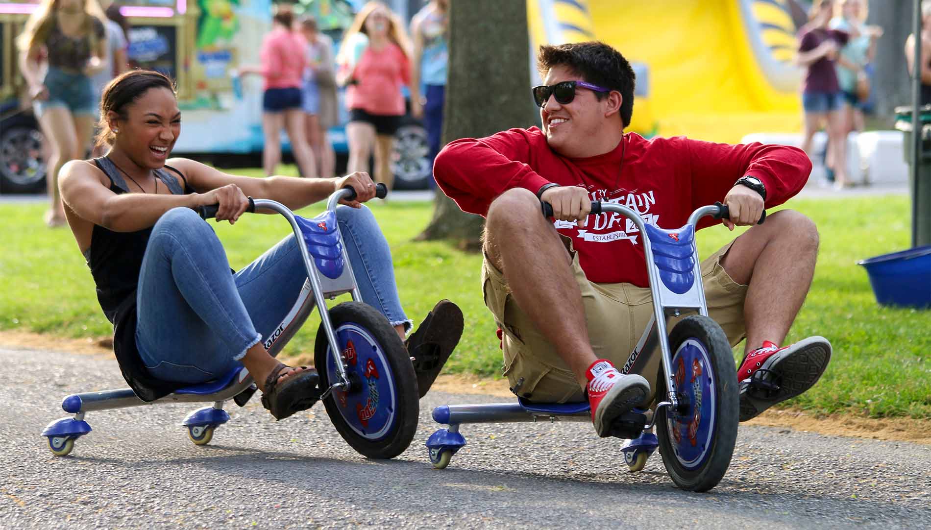 male and female students riding small tricycles and laughing